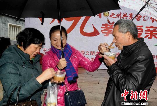 一名女青年为雨中品尝拗九粥的两位老人打伞。　记者刘可耕 摄